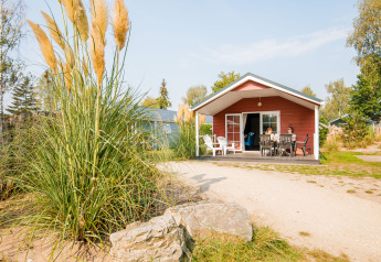 Outdoor view of a cozy red lodge with a porch, where two people are sitting at a table in the sunshine.