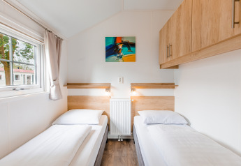 Dos camas individuales con sábanas blancas en una habitación luminosa de la Lodge en Vakantiepark Leukermeer, Países Bajos.