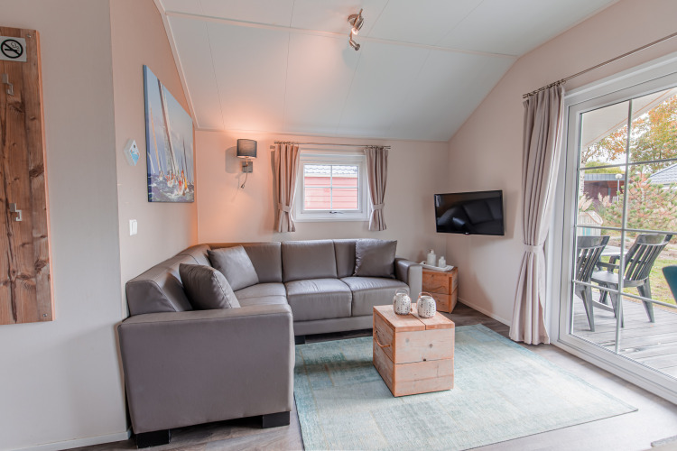 Helles Wohnzimmer in einer Lodge im Vakantiepark Leukermeer, Niederlande, mit grauem Sofa und Terrasse.