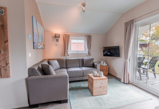 Lyst opholdsområde i Lodge på Vakantiepark Leukermeer, Holland, med grå sofa og udsigt til terrasse.