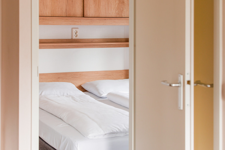 Blick in ein helles Schlafzimmer der Lodge im Vakantiepark Leukermeer in den Niederlanden mit Doppelbett.