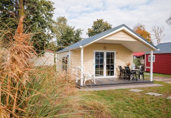 Foto af en hyggelig lodge med terrasse på Vakantiepark Leukermeer i Holland, omgivet af grønne træer.