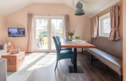 Licht, modern lodge-interieur met eettafel, bank en tv, uitkijkend op tuin in Vakantiepark Leukermeer.