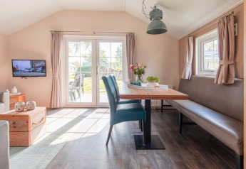 Lyst, moderne lodge-interiør med spisebord, sofa, fjernsyn og udsigt til have i Vakantiepark Leukermeer.