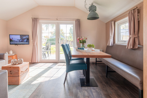 Lyst, moderne lodge-interiør med spisebord, sofa, fjernsyn og udsigt til have i Vakantiepark Leukermeer.