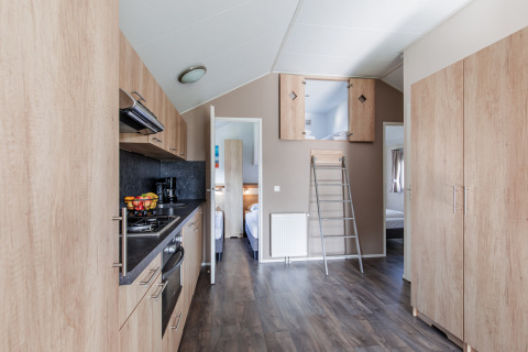 Modern lodge kitchen with wood cabinets, loft ladder, and bedroom access at Vakantiepark Leukermeer.