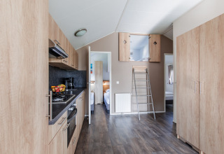 Modern lodge kitchen with wood cabinets, loft ladder, and bedroom access at Vakantiepark Leukermeer.