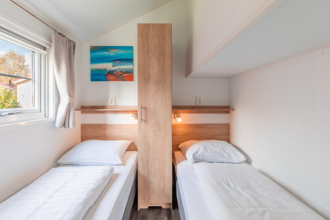 Helles, modernes Lodge-Zimmer mit zwei Einzelbetten, Holzschrank und Kunstwerk im Vakantiepark Leukermeer.