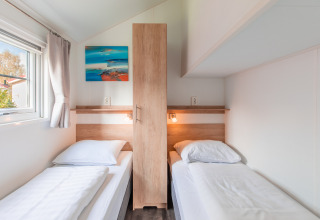 Helles, modernes Lodge-Zimmer mit zwei Einzelbetten, Holzschrank und Kunstwerk im Vakantiepark Leukermeer.
