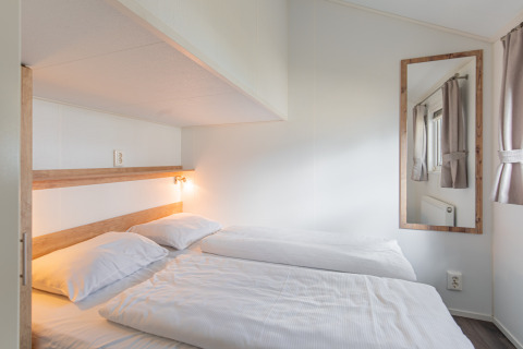 Lichte, moderne tweepersoons slaapkamer in een Lodge bij Vakantiepark Leukermeer, Nederland, met spiegel.