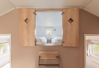 Área tipo loft con escalera y puertas de madera abiertas hacia un dormitorio con dos camas individuales.