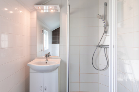 Salle de bain moderne et compacte avec douche, lavabo et miroir au Lodge | to au Vakantiepark Leukermeer, Pays-Bas.