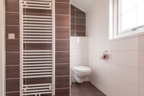 Baño moderno minimalista con inodoro suspendido, ventana y radiador toallero en Vakantiepark Leukermeer.