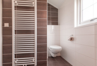 Bagno moderno minimalista con wc sospeso, finestra e scaldasalviette presso la Lodge di Vakantiepark Leukermeer.