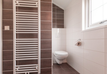 Moderne, minimalistische badkamer met zwevend toilet, raam en handdoekradiator bij Vakantiepark Leukermeer Lodge.
