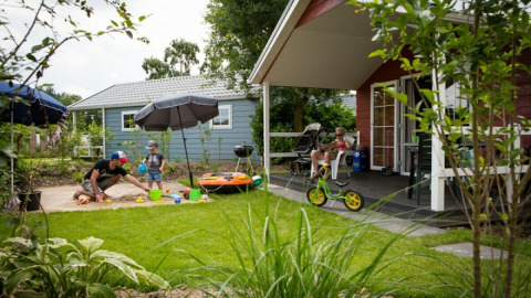 Familie genießt Sommertag vor einer Lodge im Vakantiepark Leukermeer, mit Spielplatz und Garten.