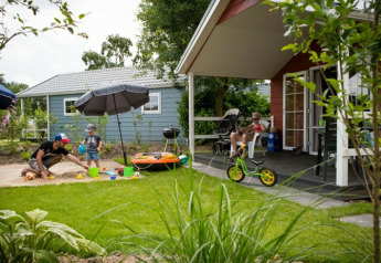 Familia disfruta de un día soleado frente a una cabaña en Vakantiepark Leukermeer, con jardín y zona de juegos.