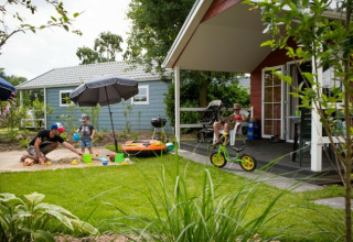 Familie nyder sommerdag foran lodge i Vakantiepark Leukermeer, med legeplads og grøn have i Holland.
