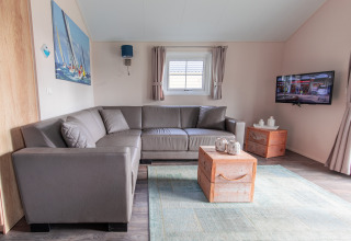 Moderne stue i Lodge på Vakantiepark Leukermeer, Holland, med hjørnesofa og fladskærms-tv på væggen.