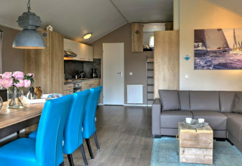 Moderne lodge-stue med turkisblå stole, gråt hjørnesofa, træbord og lyst køkken i Vakantiepark Leukermeer.