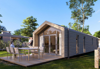 Modern strandhuis van hout met terras en eettafel buiten, omgeven door bomen en een groene omgeving.