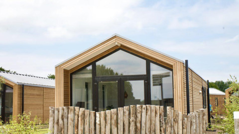 Moderne houten lodge met grote ramen en rustiek hekwerk bij Beach House Zuid, EuroParcs Enkhuizer Strand, Nederland.