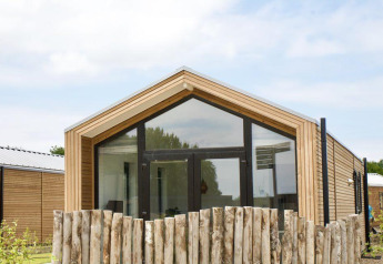 Moderne houten lodge met grote ramen en rustiek hekwerk bij Beach House Zuid, EuroParcs Enkhuizer Strand, Nederland.