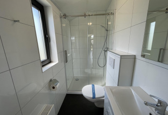 Moderne badkamer met douche, toilet en raam in Beach House Zuid, EuroParcs Enkhuizer Strand, Nederland.