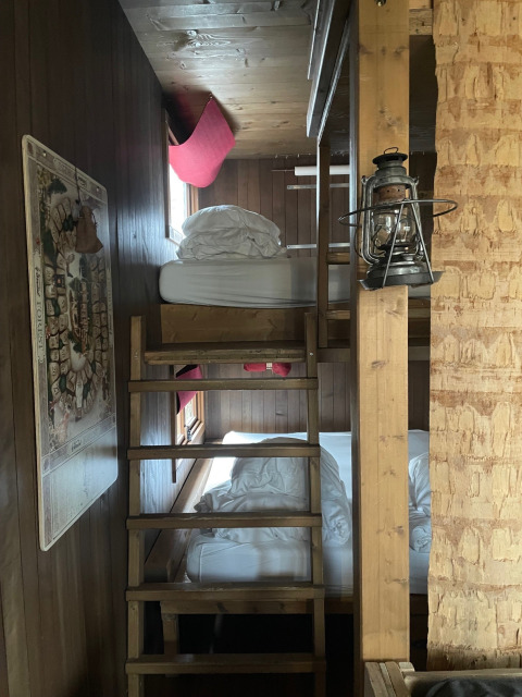 Gezellige boomhutkamer met houten stapelbedden, ramen, een lantaarn en een kaart aan de muur.