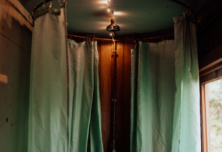 Knusse douche met groene gordijnen en warme lichtjes in een houten lodge met een raam ernaast.