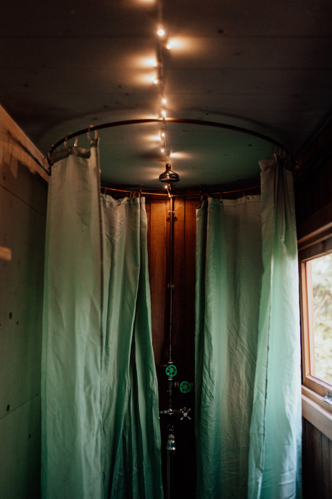 Douche chaleureuse avec rideaux verts et guirlande lumineuse dans un lodge rustique en bois avec fenêtre。