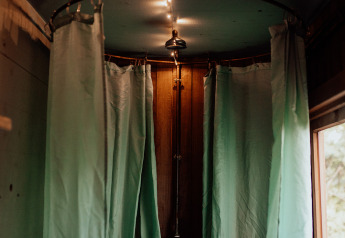 Ducha acogedora con cortinas verdes y luces tenues en una cabaña rústica de madera junto a una ventana。