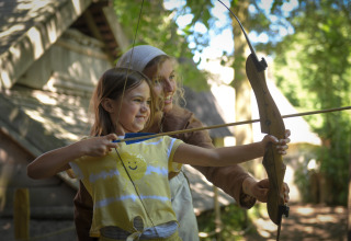 Niña y adulta practicando tiro con arco frente a una tienda safari en Lodgetent Archeon Expedition, Países Bajos.