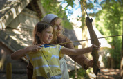 Niña y adulta practicando tiro con arco frente a una tienda safari en Lodgetent Archeon Expedition, Países Bajos.
