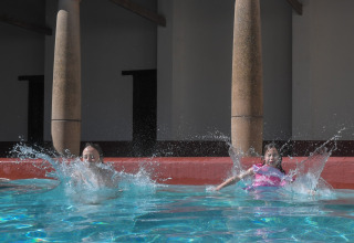 Due bambini fanno splash in piscina davanti alle colonne a Lodgetent Archeon Expedition, Paesi Bassi.