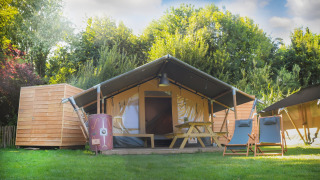 Tente safari Lodgetent Archeon Expedition avec terrasse en bois, table et chaises, entourée de verdure.