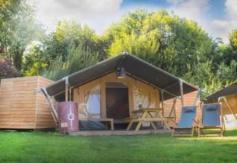 Safari telt Lodgetent Archeon Expedition med træterrasse, bord og stole foran, placeret i grøn natur.