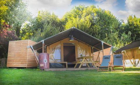 Tenda safari Lodgetent Archeon Expedition con terrazza in legno, tavolo e sedie, immersa nel verde.