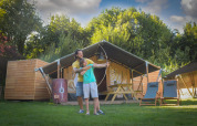 Un adulto ayuda a un niño con el tiro con arco frente a una tienda safari en Lodgetent Archeon Expedition.