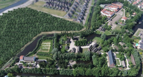 Luchtfoto van Camping Expeditie Archeon met tenten en historische gebouwen, omgeven door groen en water.