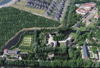 Vista aerea del Camping Spedizione Archeon con tende e edifici storici circondati da foresta e acqua.