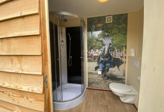 Badeværelse i Lodgetent Archeon Expedition med brusekabine, toilet og ridderkunst på væggen.