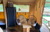 Interior de la tienda safari Lodgetent Archeon Expedition con sillas acogedoras y mesa de madera.
