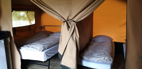 Interieur van Lodgetent Archeon Expedition safaritent met drie aparte bedden en gordijnen voor privacy.