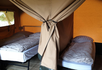 Interieur van Lodgetent Archeon Expedition safaritent met drie aparte bedden en gordijnen voor privacy.
