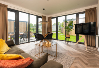 Wohnzimmer der Oak Lodge mit großen Fenstern, moderner Einrichtung und Blick ins Grüne in den Niederlanden.