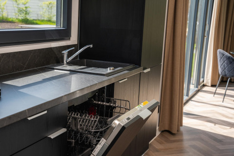 Modern lodge kitchen with open dishwasher, black cabinets, marble countertop, and view of the garden.