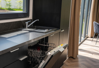 Moderne lodgekeuken met open vaatwasser, zwart werkblad, marmeren blad en zicht op de tuin.