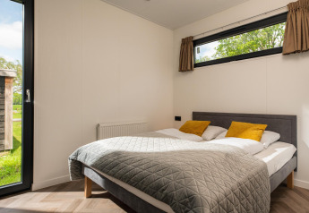 Camera moderna presso Oak Lodge con letto matrimoniale, cuscini gialli, grandi finestre e vista sul verde.