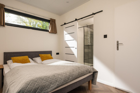 Modern bedroom in Oak Lodge at Vakantiepark Hölte, Netherlands, featuring an ensuite bathroom and window.